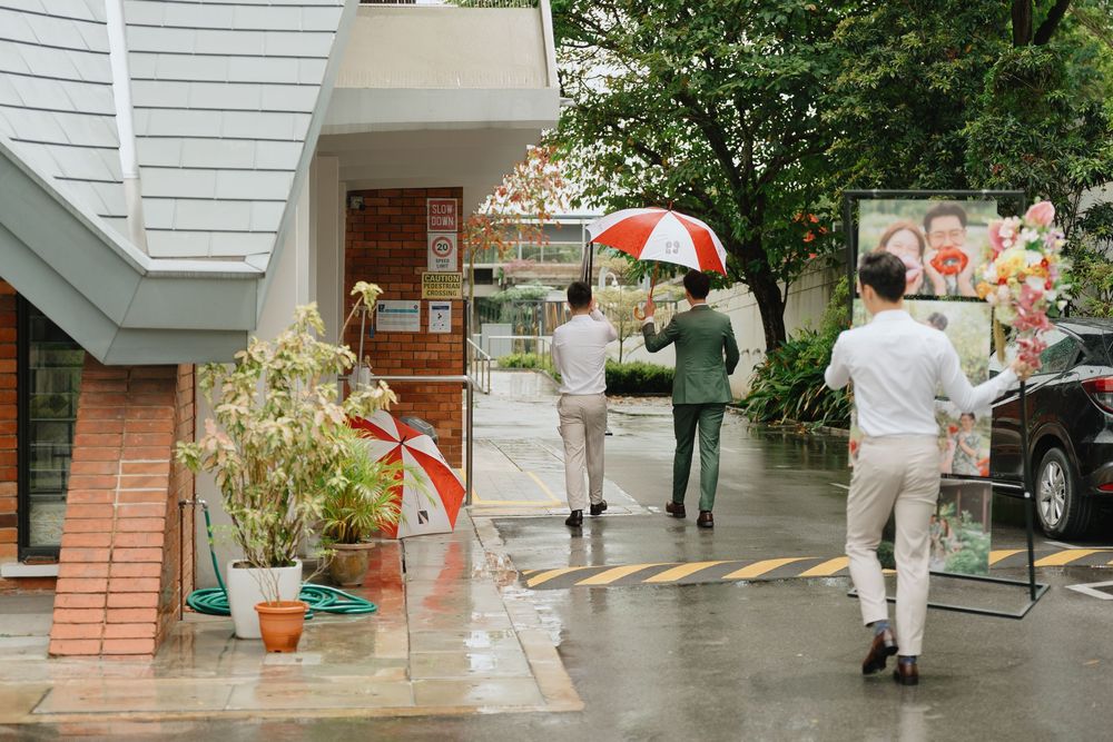 People walking with red umbrella in rain outside a building.