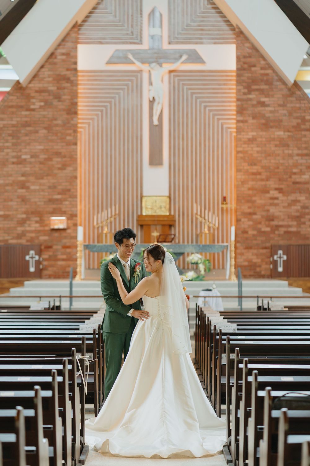A bride and groom share a romantic moment at the altar of a elegant brick church with a crucifix backdrop.