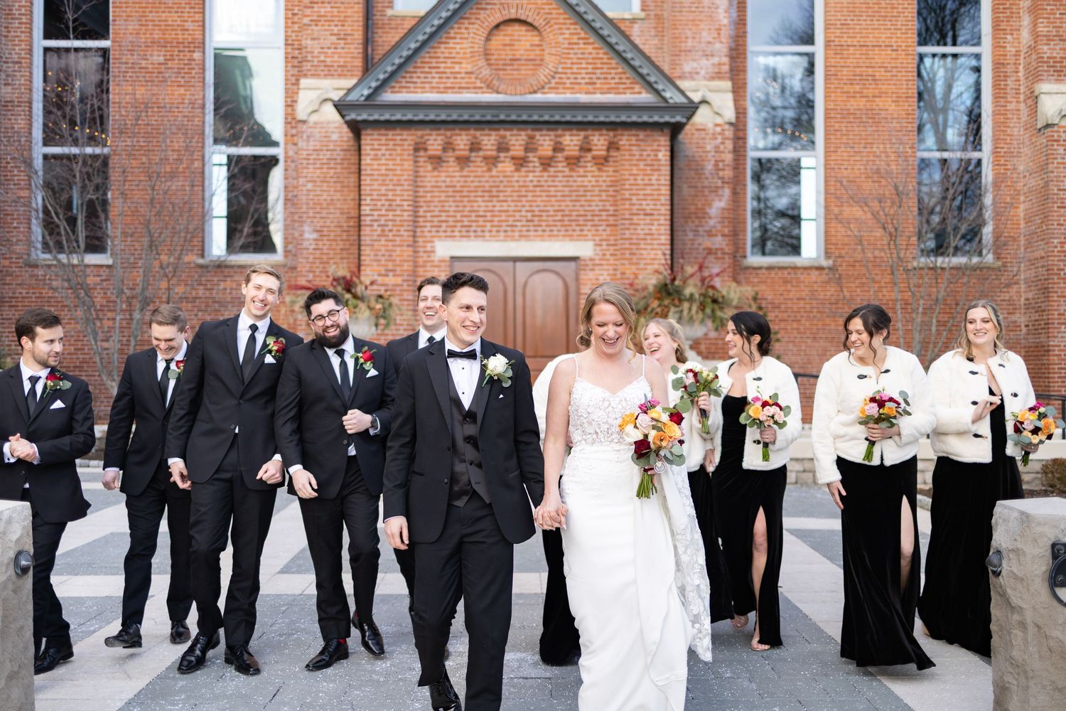 Wedding party walks outside the Monastery, bride and groom holding hands, groomsmen in black suits, bridesmaids in black gowns.