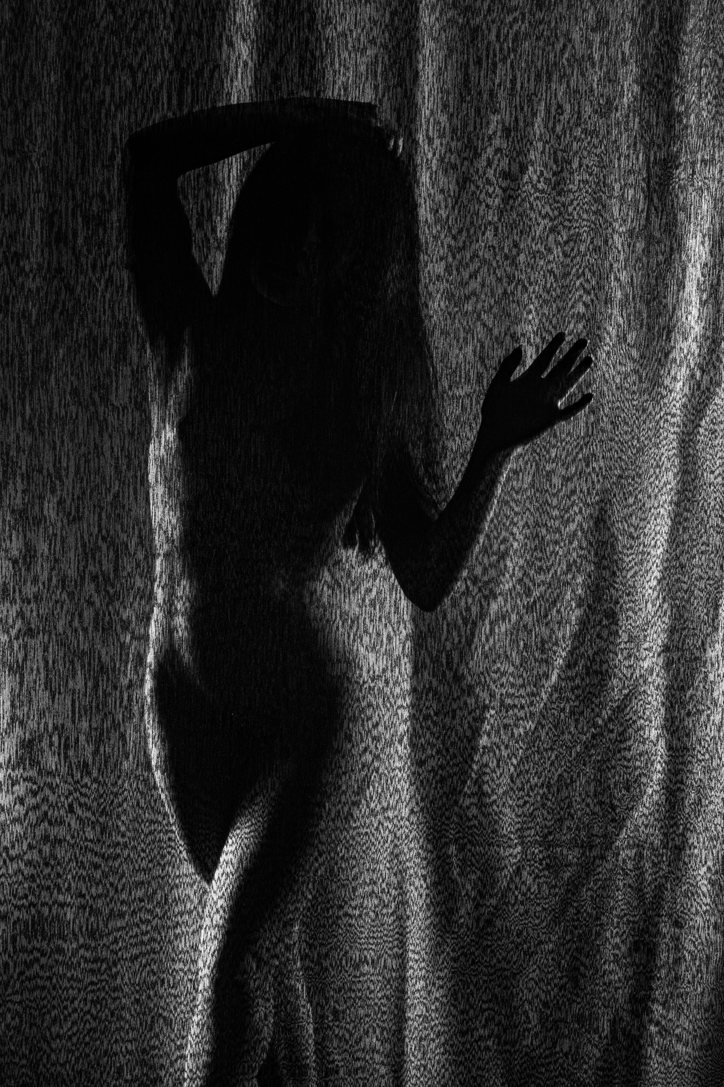 Silueta boudoir en blanco y negro a través de cortina texturizada. Fotografía artística de desnudo con contraluz y sombras.