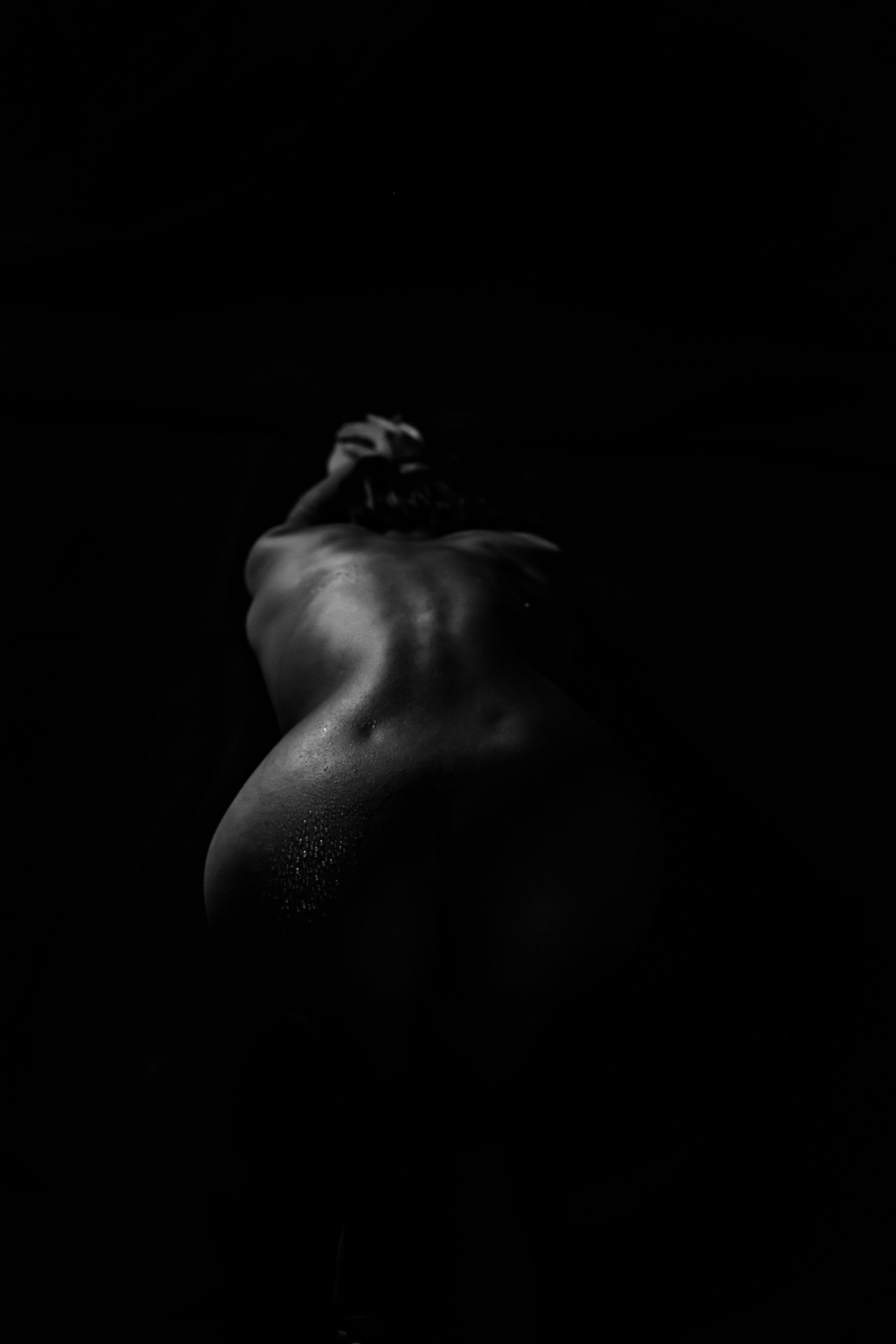 Fotografía artística en blanco y negro de la espalda y silueta femenina. Perspectiva longitudinal con iluminación sutil sobre fondo negro