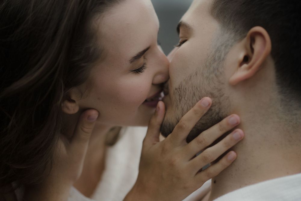 A romantic couple sharing a tender kiss, with the woman gently holding the man's face in an intimate moment.