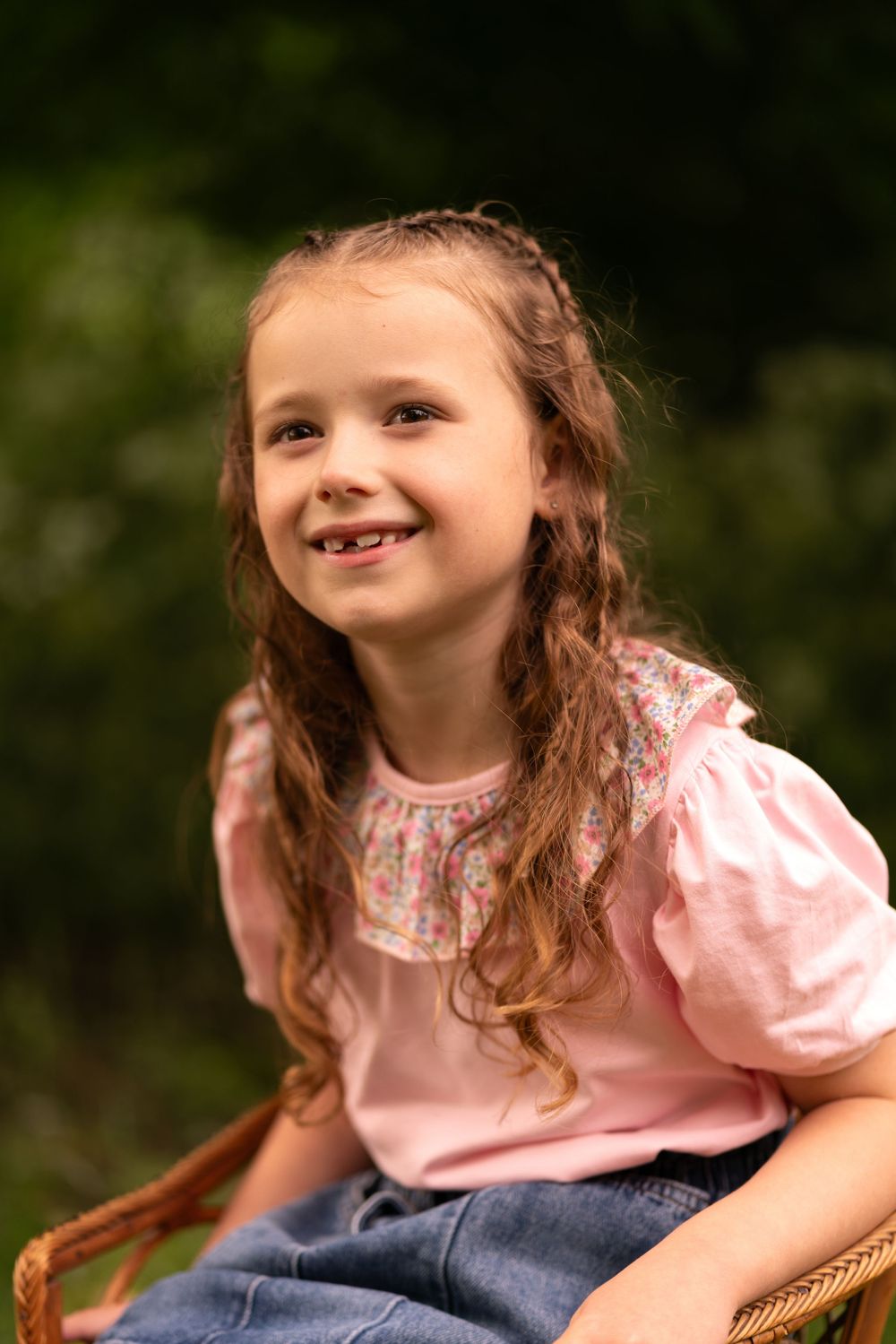 A smiling young girl with curly hair sitting outdoors during a childhood photography session in Lincolnshire.