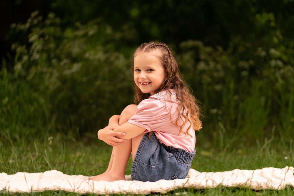 Young girl with curly hair sitting on a blanket outdoors, smiling over her shoulder during a childhood photoshoot in Lincolnshire.