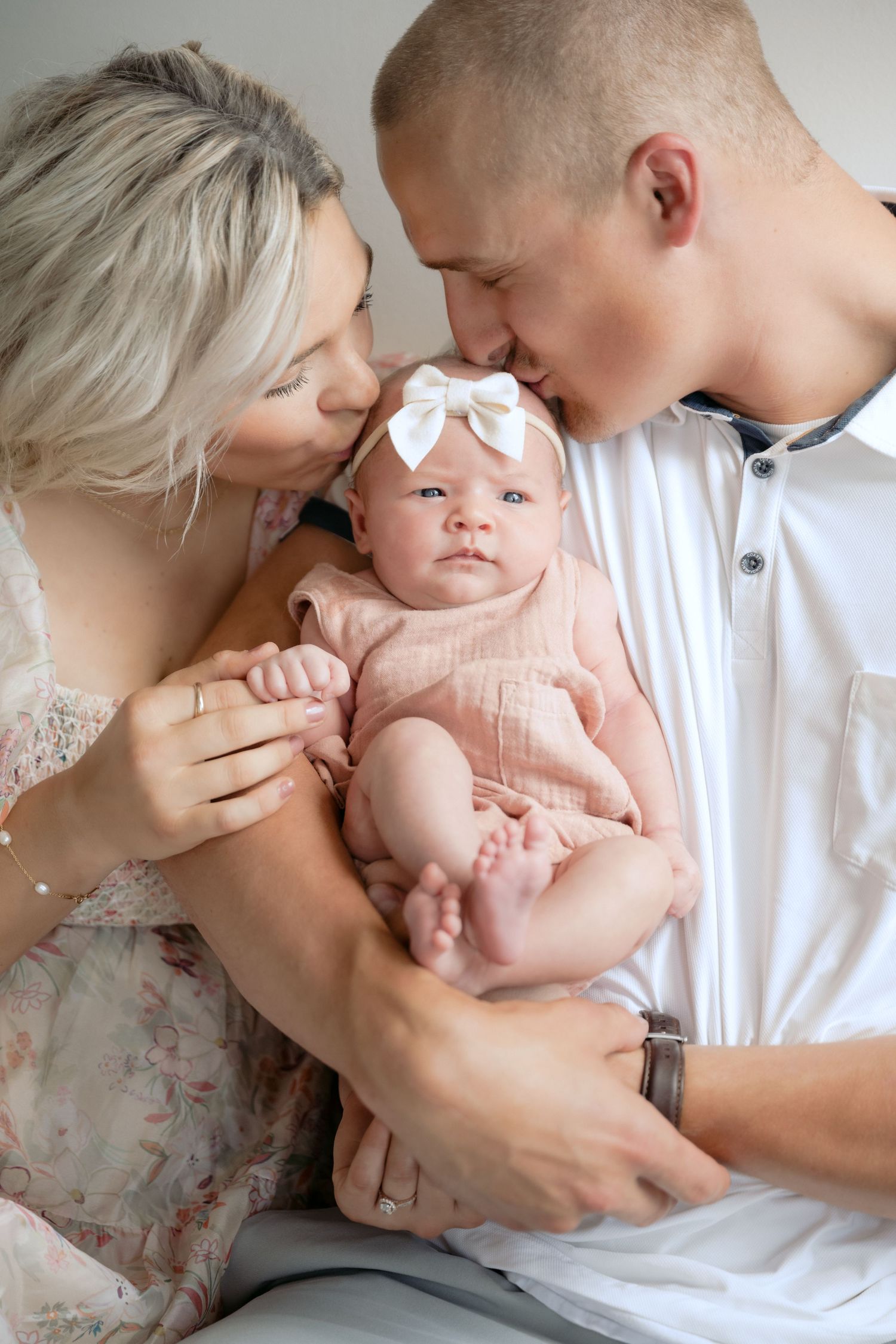 parents kissing newborn baby's head while baby looks towards the camera during in-studio lifestyle newborn session in stillwater, mn