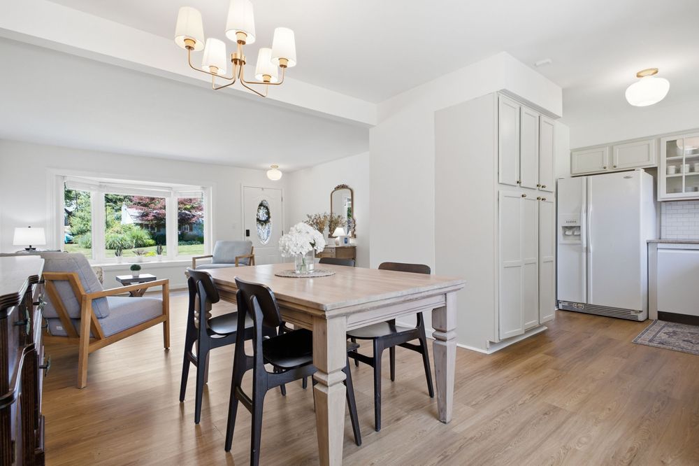 Bright dining room with wooden table, black chairs, hardwood floors, white cabinetry, and chandelier lighting.