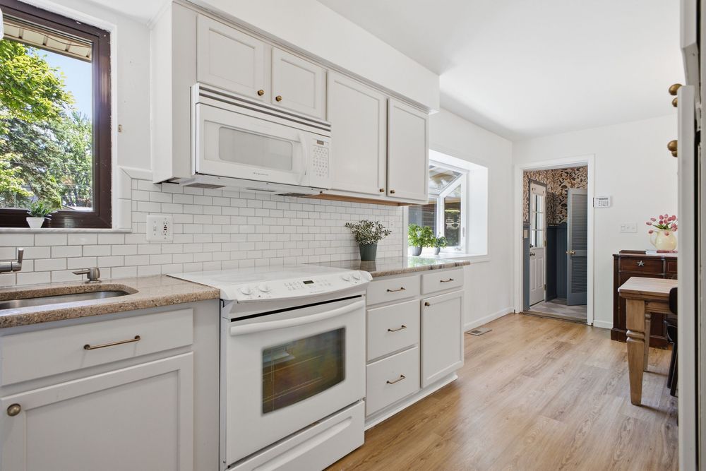 Bright kitchen with white cabinets, subway tile backsplash, white appliances, and hardwood floors.