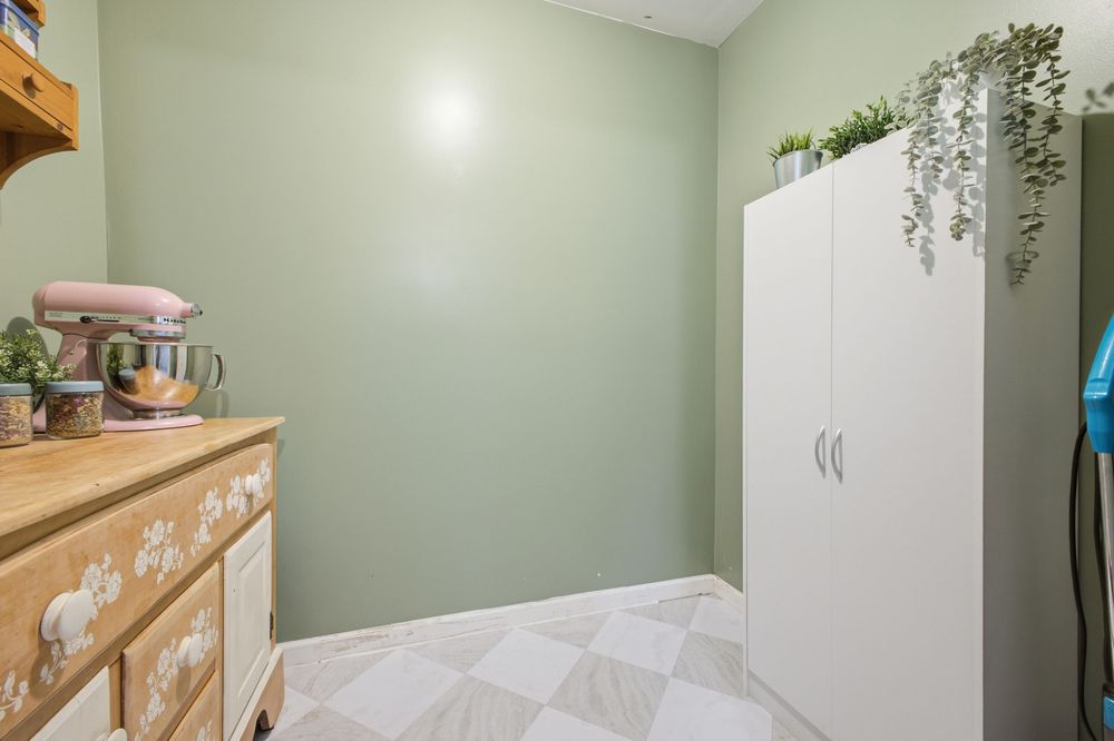 Laundry room with sage green walls, white storage cabinet, wooden dresser, and checkered tile flooring.