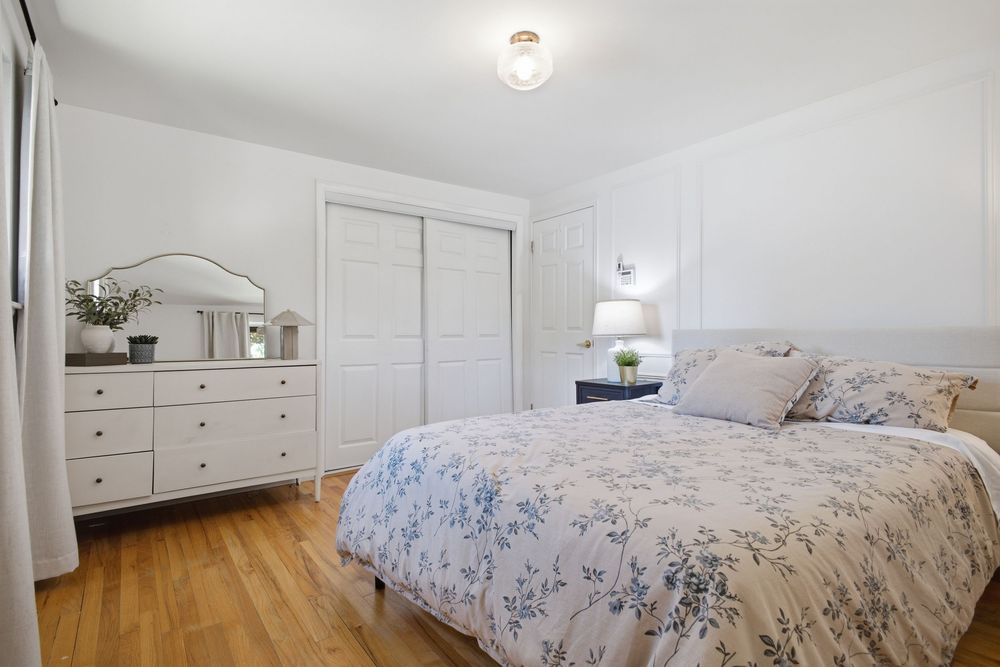 Cozy bedroom with floral bedding, white dresser, closet doors, and light hardwood floors.