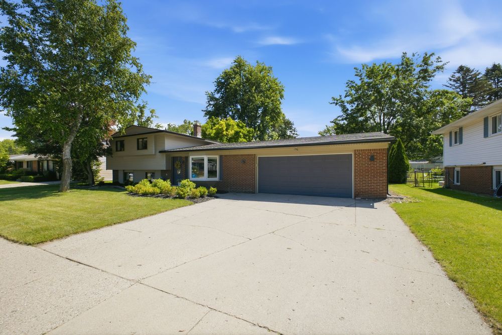 Ranch-style home with attached two-car garage, wide concrete driveway, and mature trees on a well-maintained green lawn.