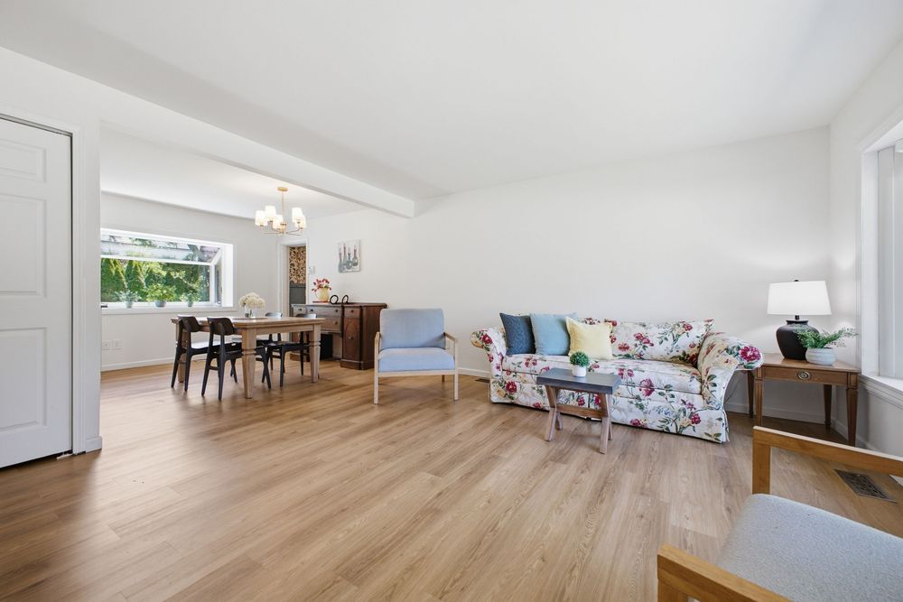 Bright open-plan living room with floral sofa, hardwood floors, and dining area with chandelier.