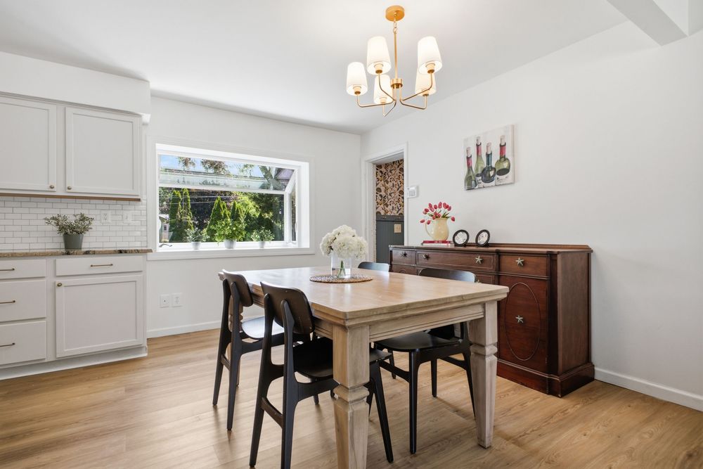 Bright dining room with wood table, black chairs, chandelier, white cabinets, and hardwood floors.