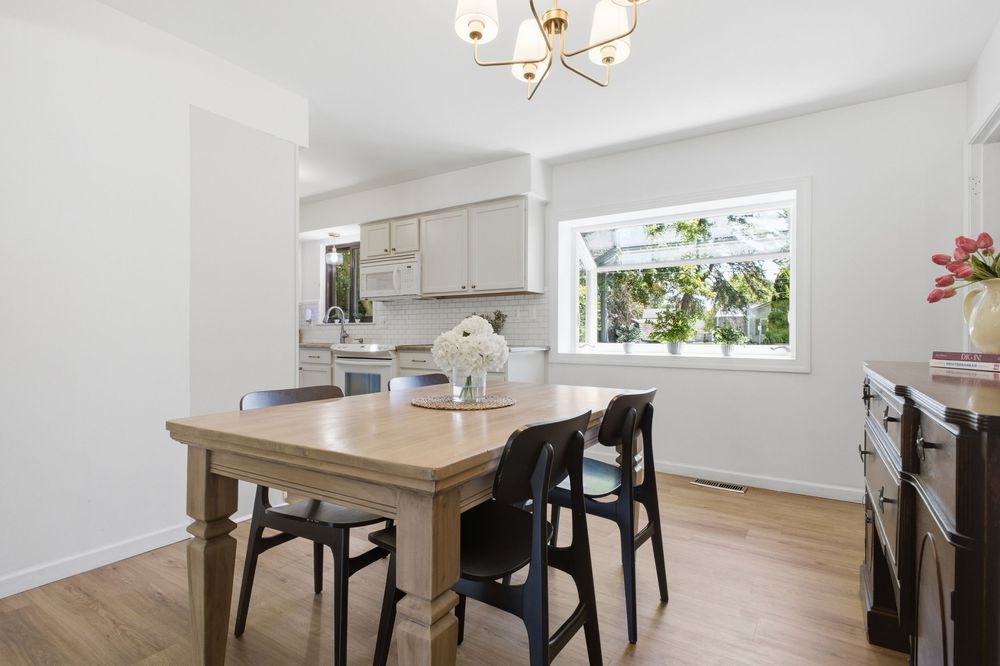 Airy dining area featuring a wooden table, black chairs, chandelier, and large window with garden views.