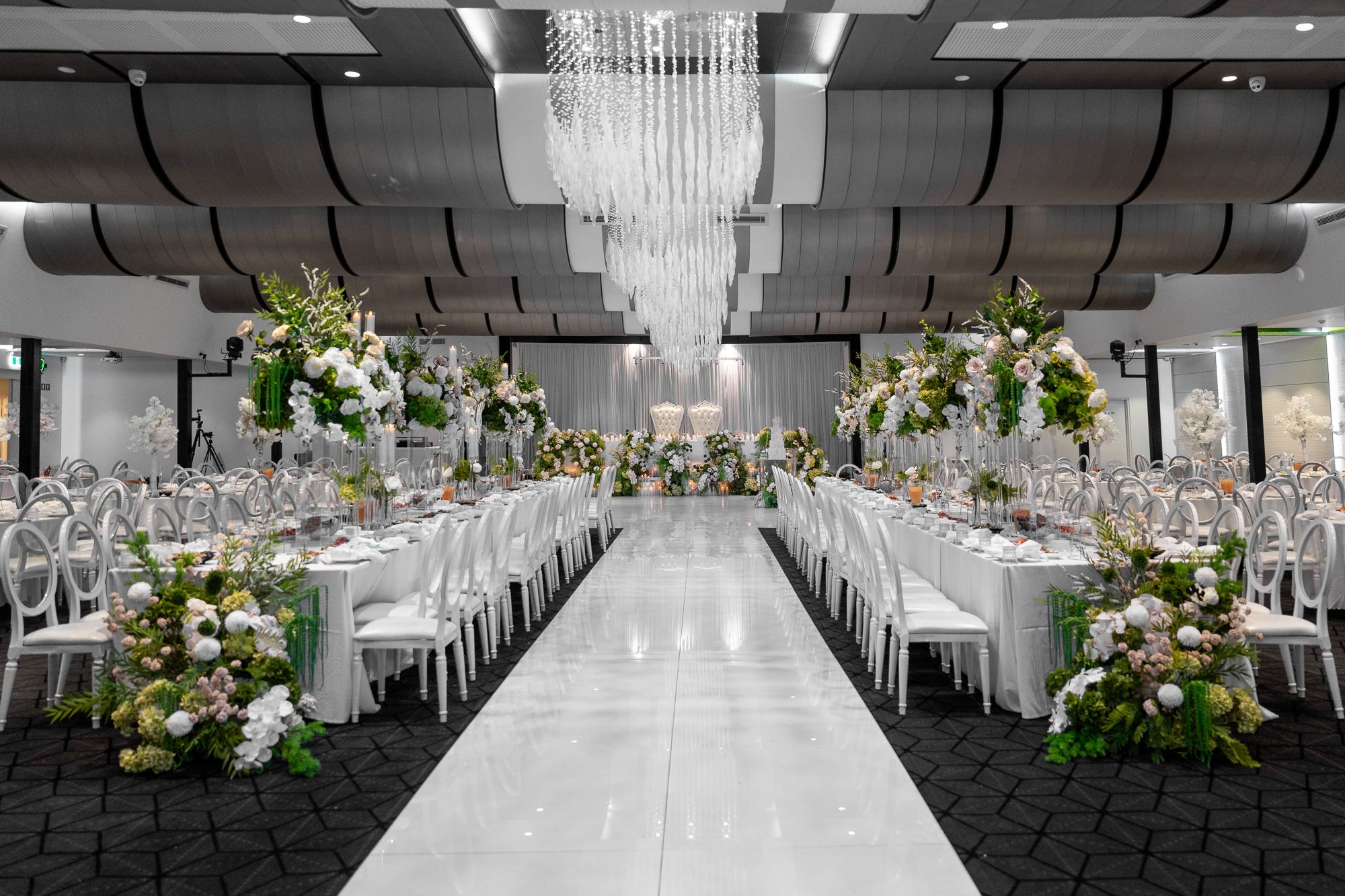 Modern wedding venue with crystal chandeliers and symmetrical table arrangements.