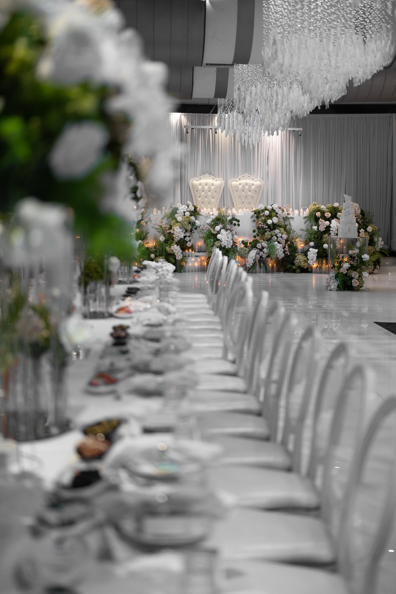 Wedding reception tables set with crystal decor and white floral arrangements under dramatic lighting.