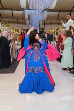 Performer in vibrant blue and pink traditional costume dancing at a wedding celebration.