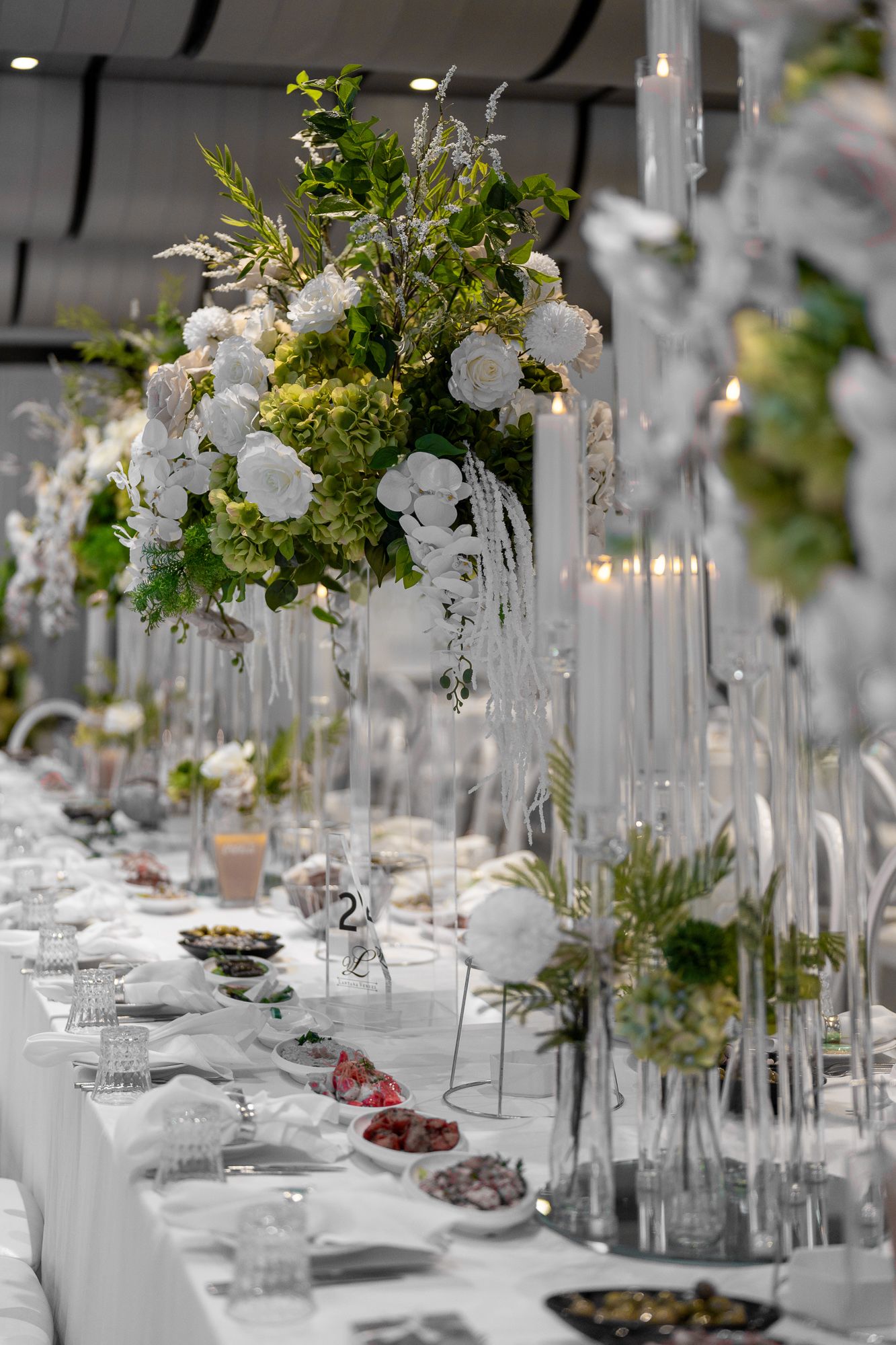 Long banquet tables decorated with white floral centerpieces and crystal vases for an elegant wedding reception.