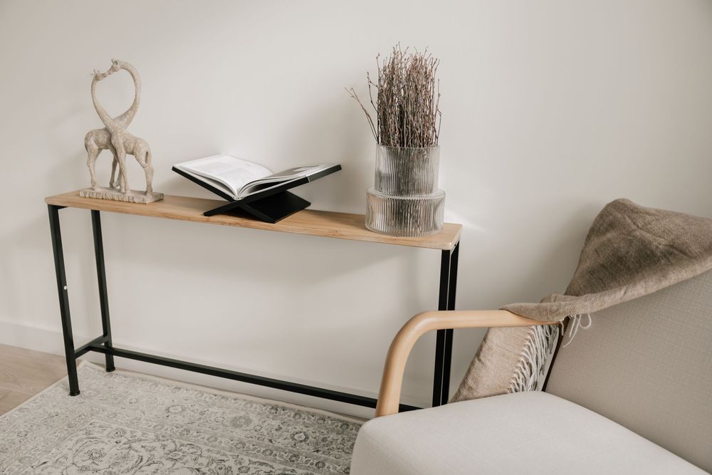 Modern minimalist console table with black metal frame and wood top, styled with decor against neutral wall.
