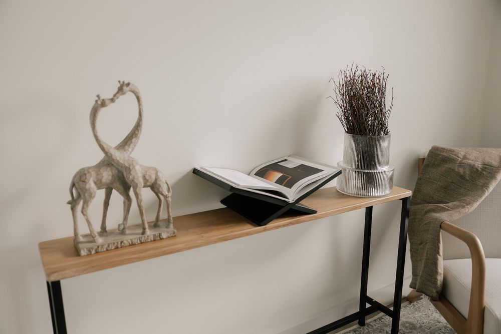 Minimal home decor featuring a giraffe sculpture, open book, and potted plant on a wooden console table with metal legs.
