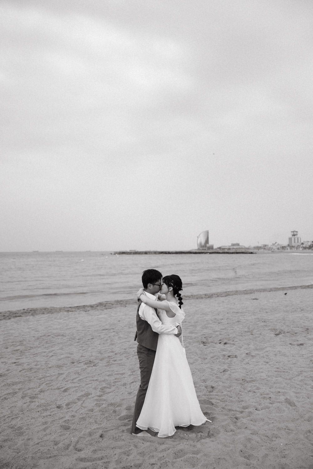 Black and white photo of a couple sharing an intimate moment on an empty beach.