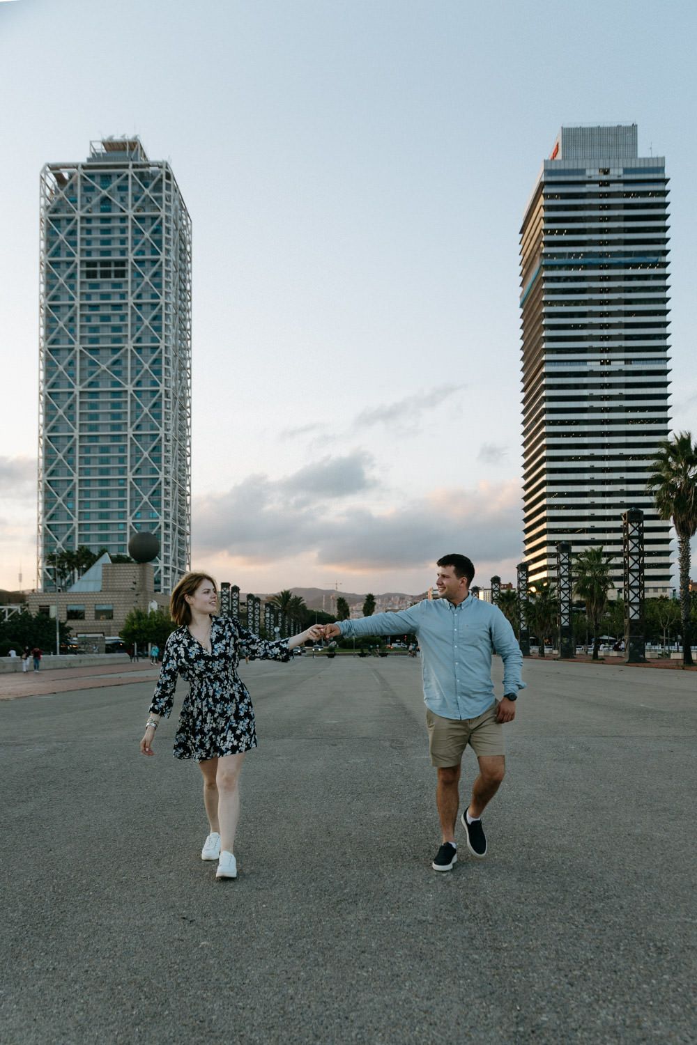 Couple walks holding hands between modern skyscrapers in city.