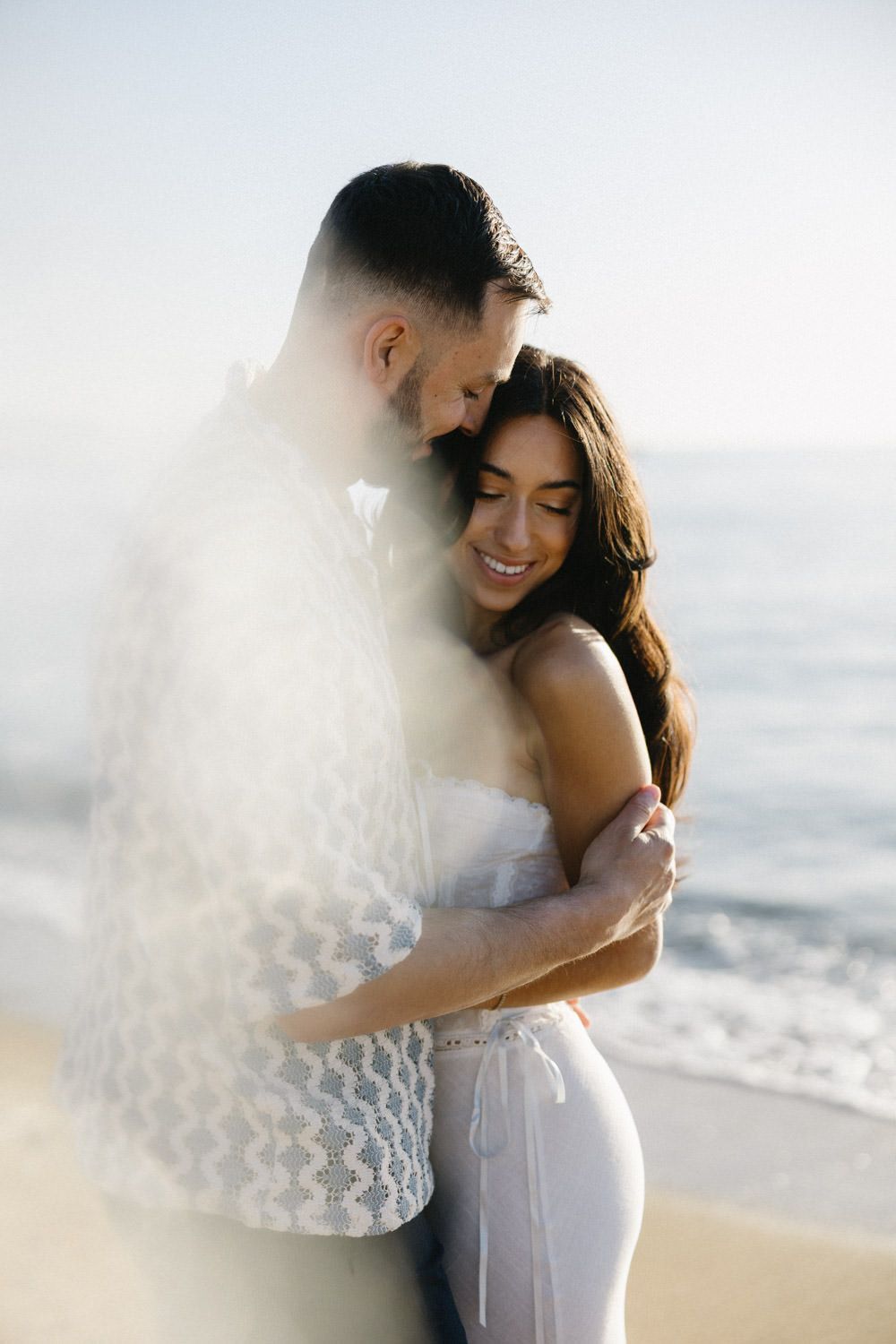 Intimate beach maternity photos with soft ethereal lighting and ocean backdrop.