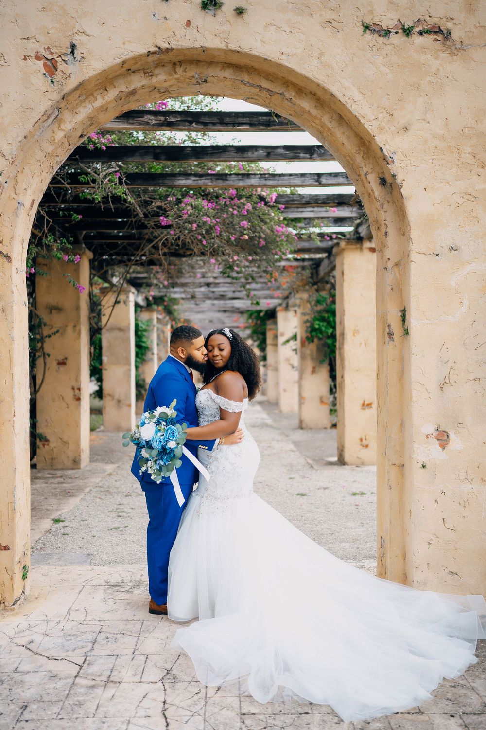 A couple poses under stone archways with flowering vines at a Mediterranean-style wedding venue.