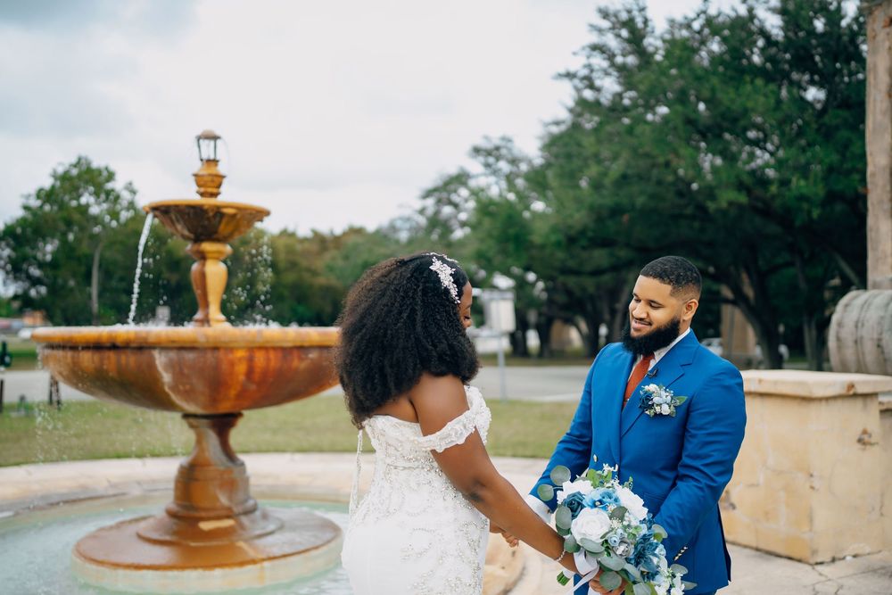 A couple shares a joyful moment by a gold-toned fountain during their outdoor wedding celebration.