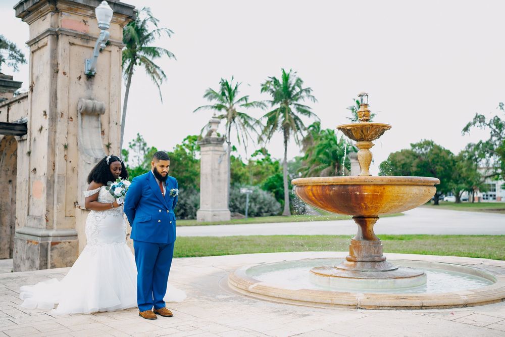 Newlyweds pose for wedding photos near an ornate golden fountain with palm trees in the background.