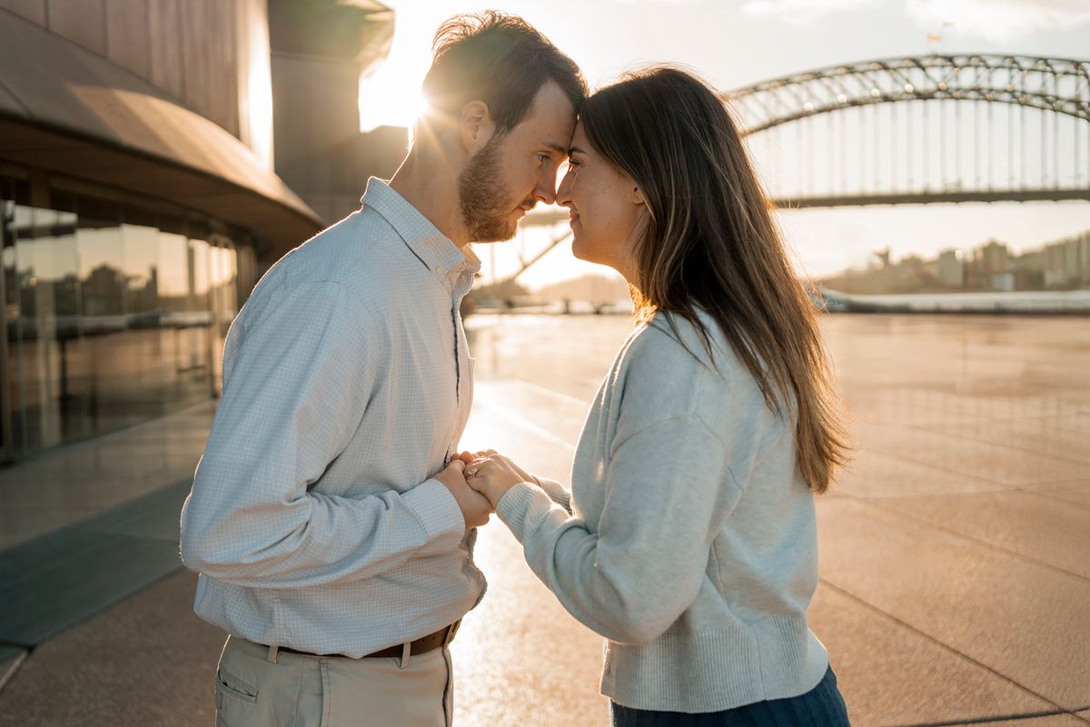 couple touches forehead to forehead romantically with the setting sun behind them shining in Sydney proposal photography
