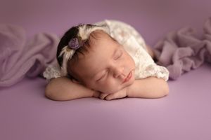 Artistic newborn photography series with baby sleeping on lavender colored background.