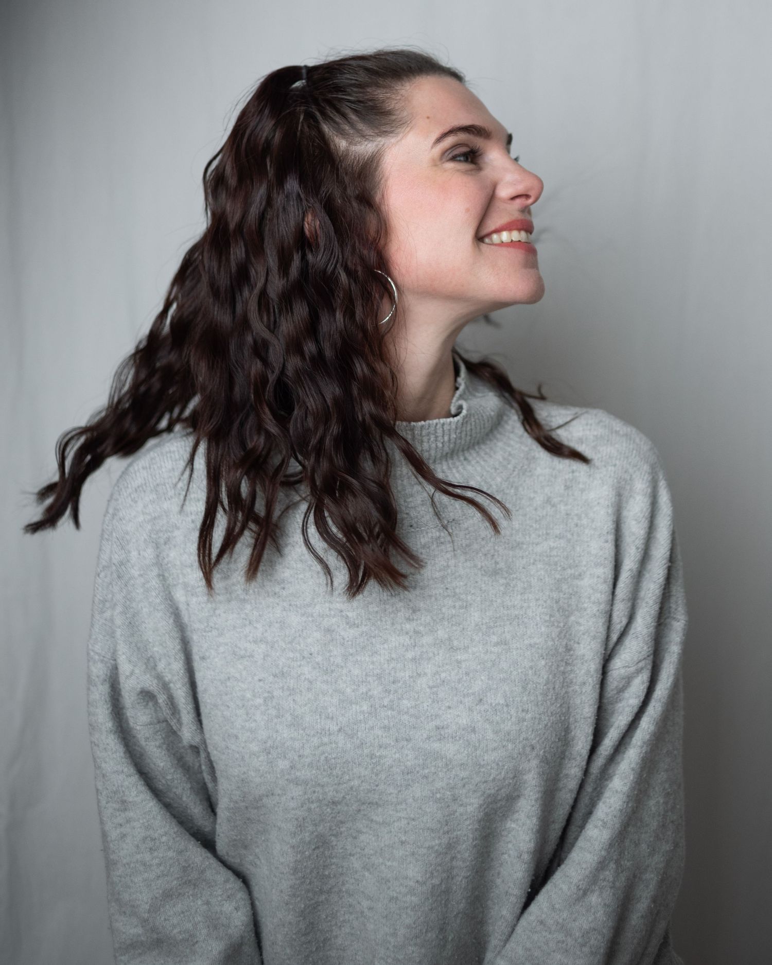 A sequence of shots showing a person with dark wavy hair wearing a grey sweater making dynamic movements against a grey wall.