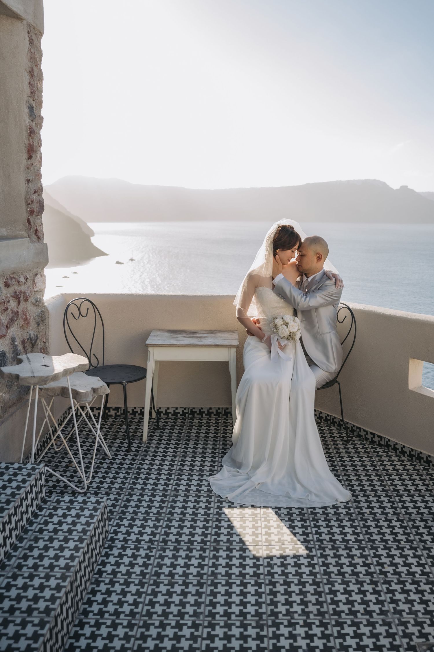 A romantic wedding moment on a Santorini terrace with patterned tile flooring overlooking a scenic coastal view.