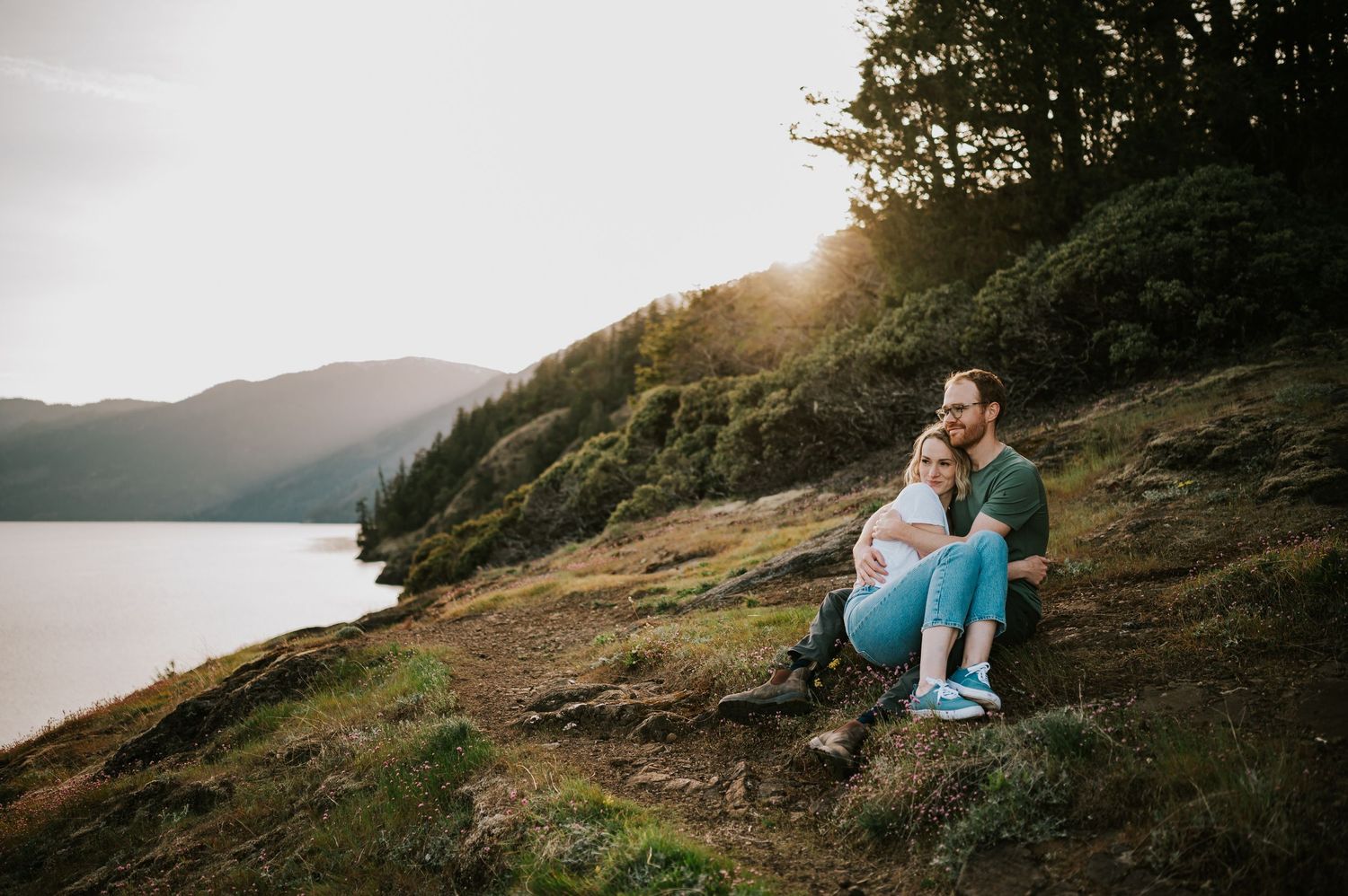 Romantic moment between a couple during their Vancouver Island engagement session sitting on the Comox Lake bluff during golden hour