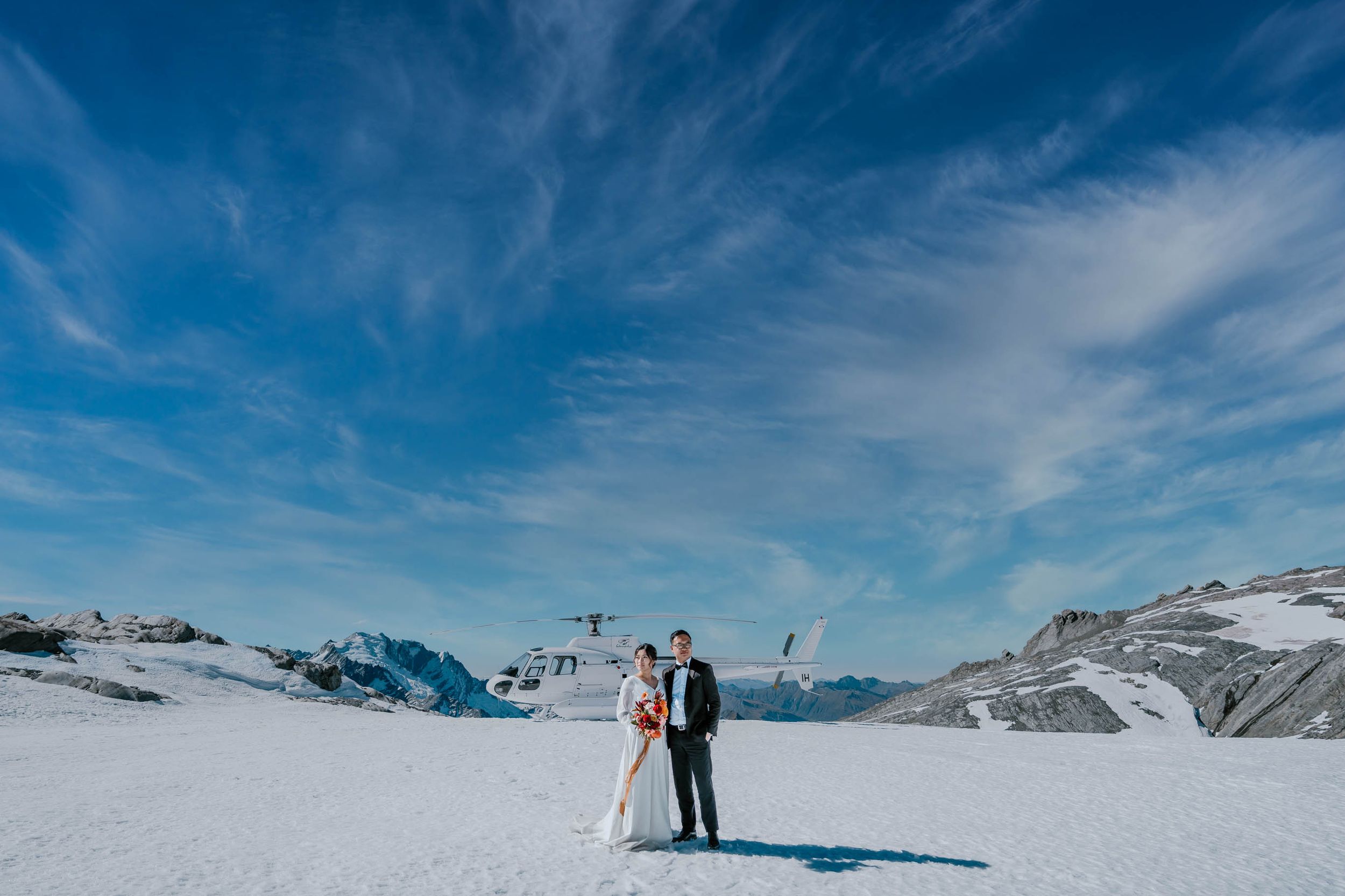 Wedding Photography Sydney A couple poses on a snowy mountain peak with dramatic blue skies and snow-capped peaks in the background.