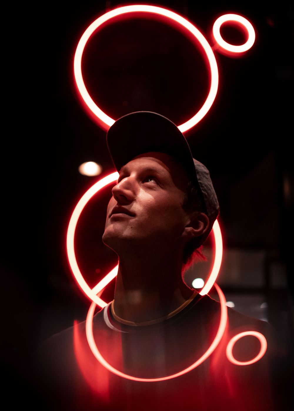A figure is illuminated by glowing red neon circles and curves in a dark setting creating a dramatic lighting effect.