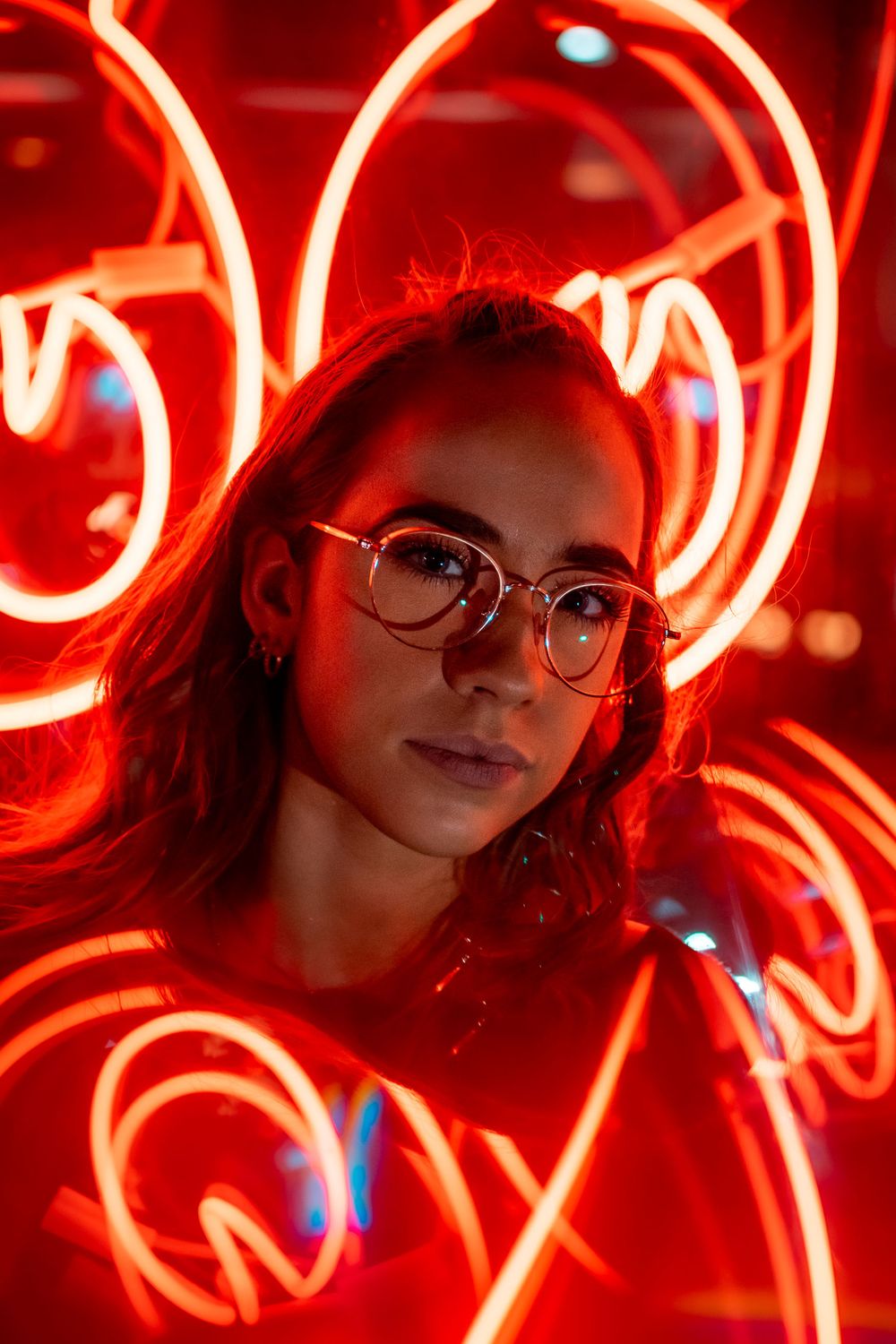 A series of portraits bathed in red neon light showing a person wearing round glasses.