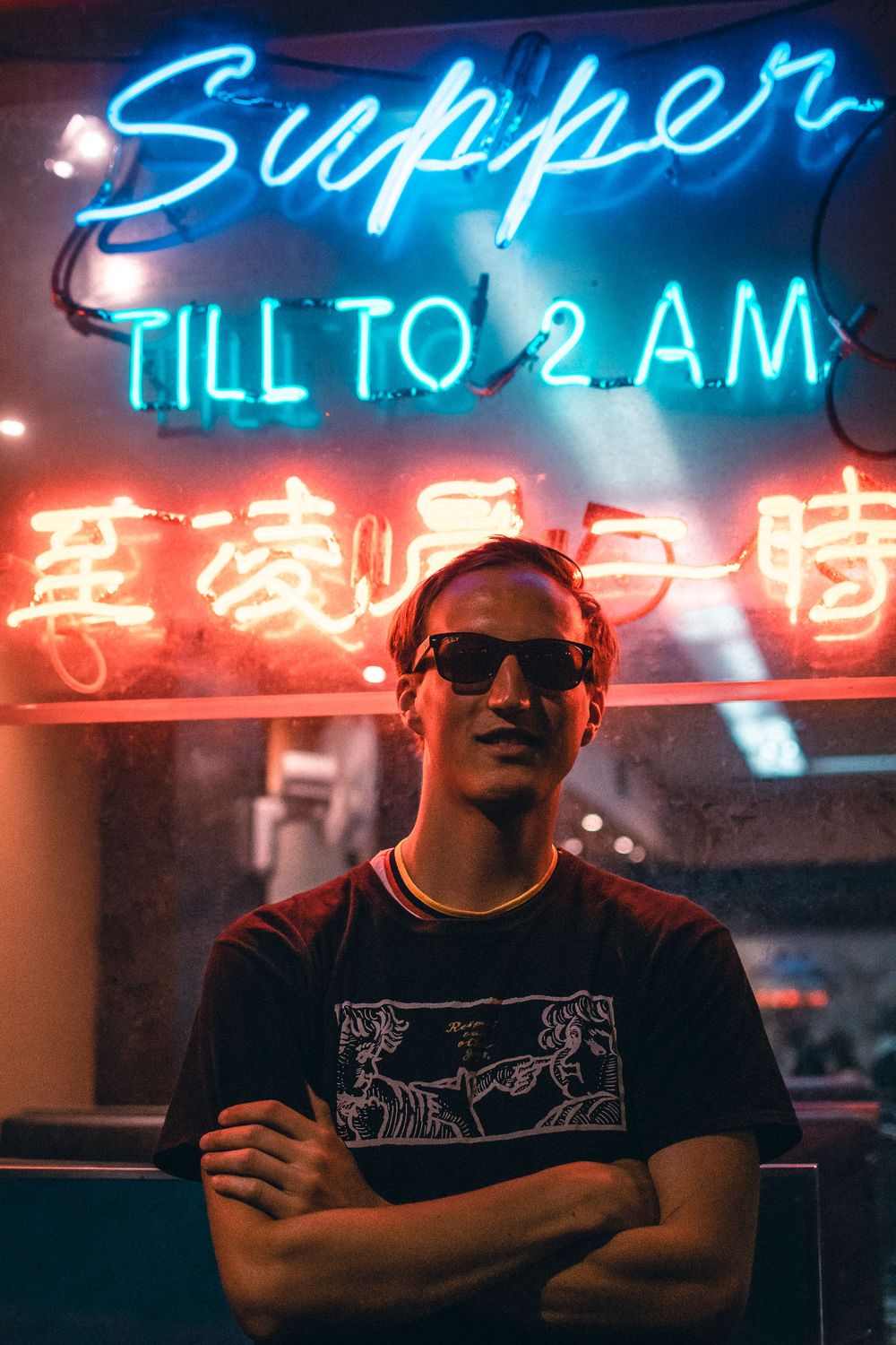 Neon signs illuminate a moody nighttime scene with blue and red lighting creating an atmospheric urban ambiance.