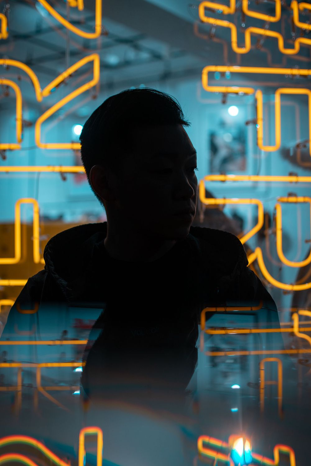 Silhouetted figures sit against a backdrop of glowing orange geometric patterns in a dark room.