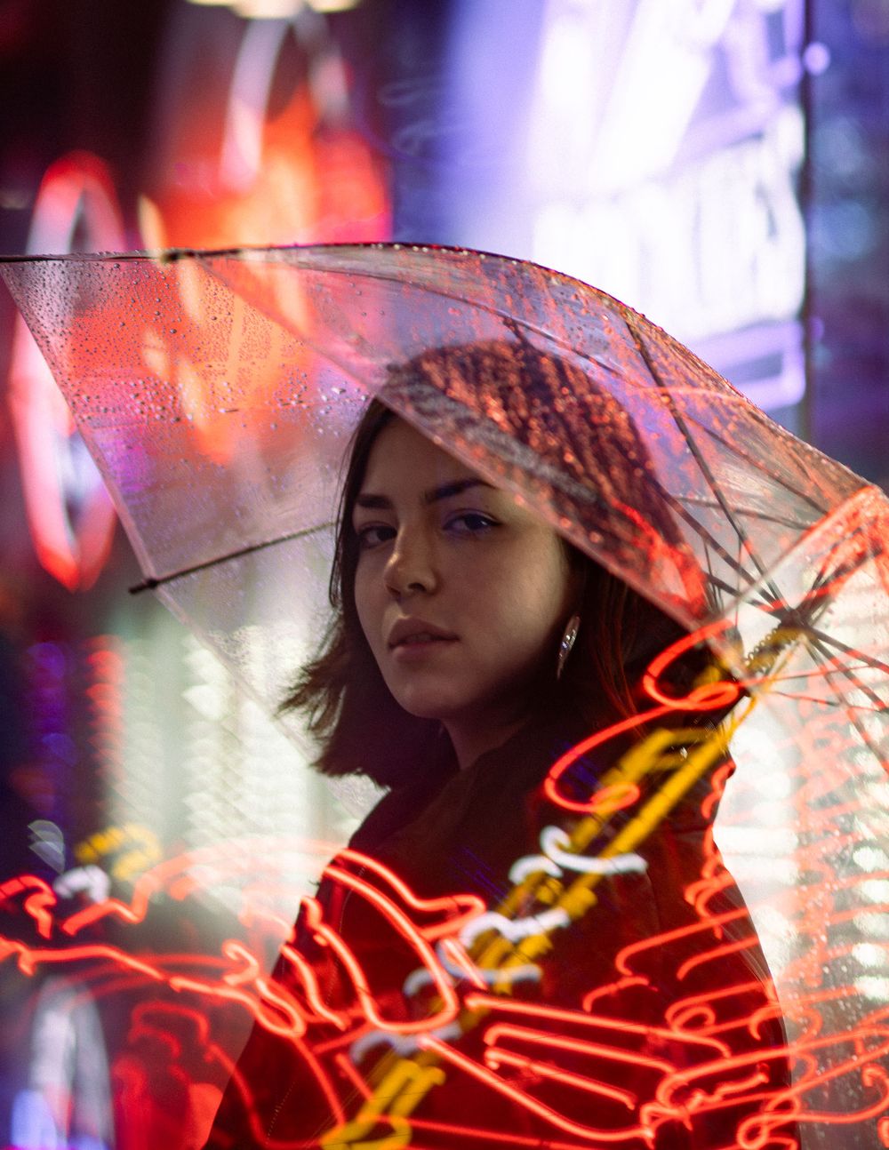 Person holding a clear umbrella against neon lights creating a moody urban nighttime atmosphere.