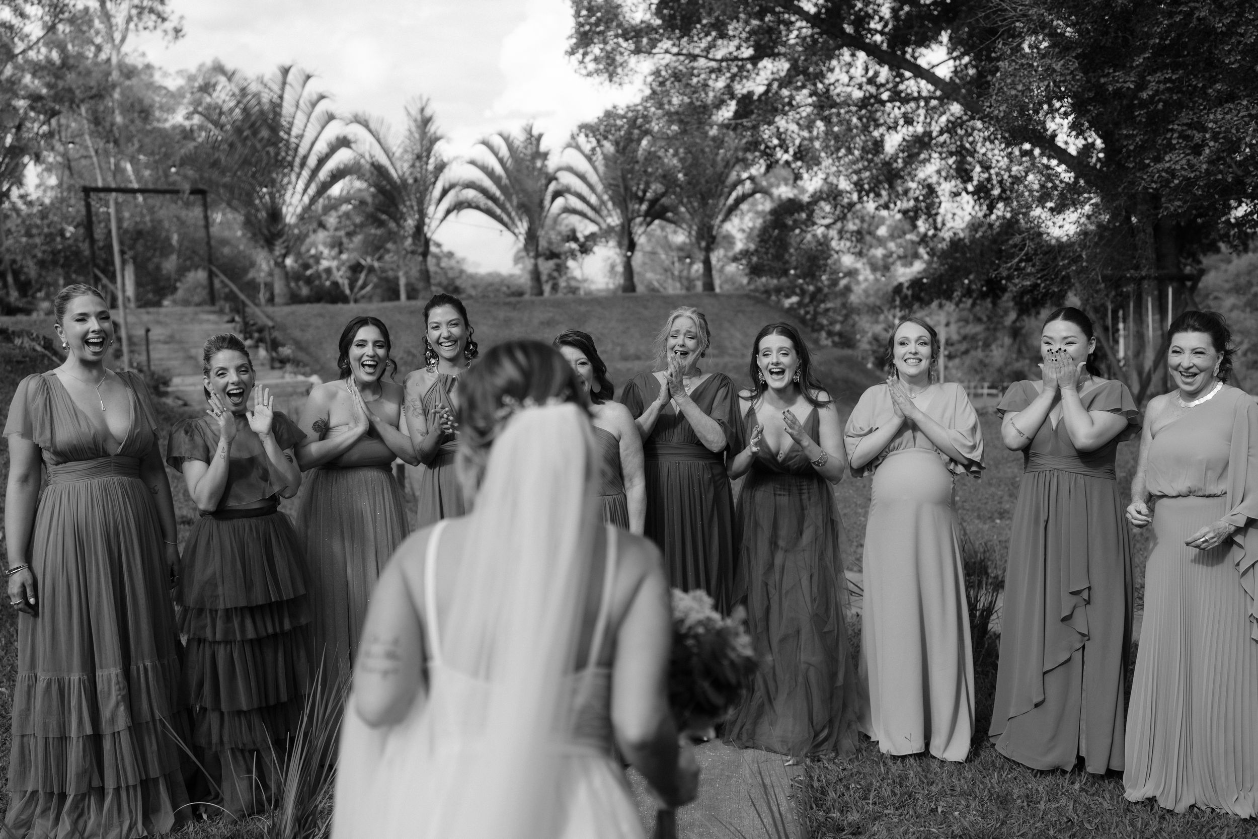 Wedding party wearing coordinated gray dresses stands together outdoors for group photo.