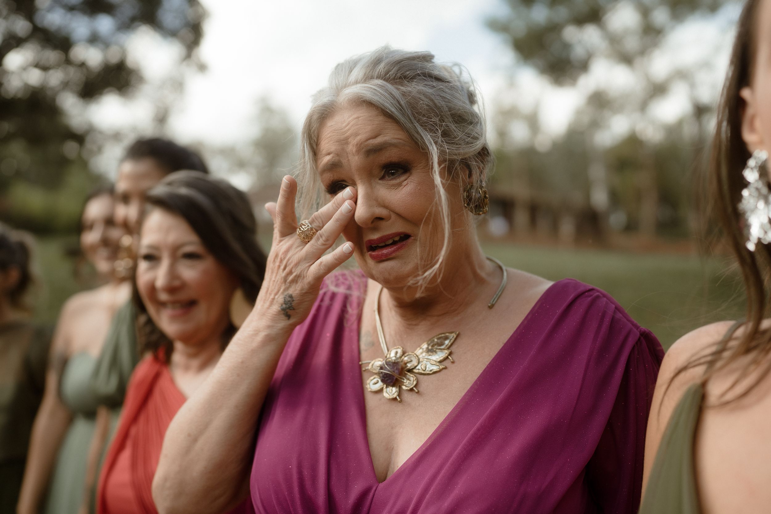 Bridesmaids in burgundy dresses share joyful candid moments during outdoor celebration.