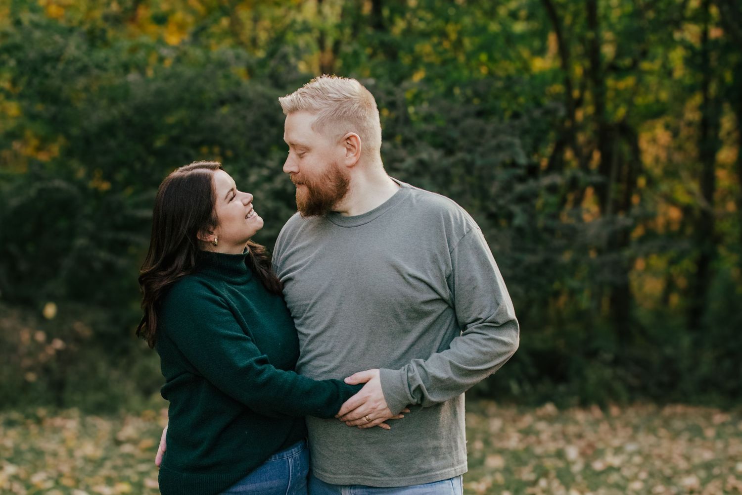 Couple embracing and smiling at each other outdoors in autumn forest with colorful fall foliage background.