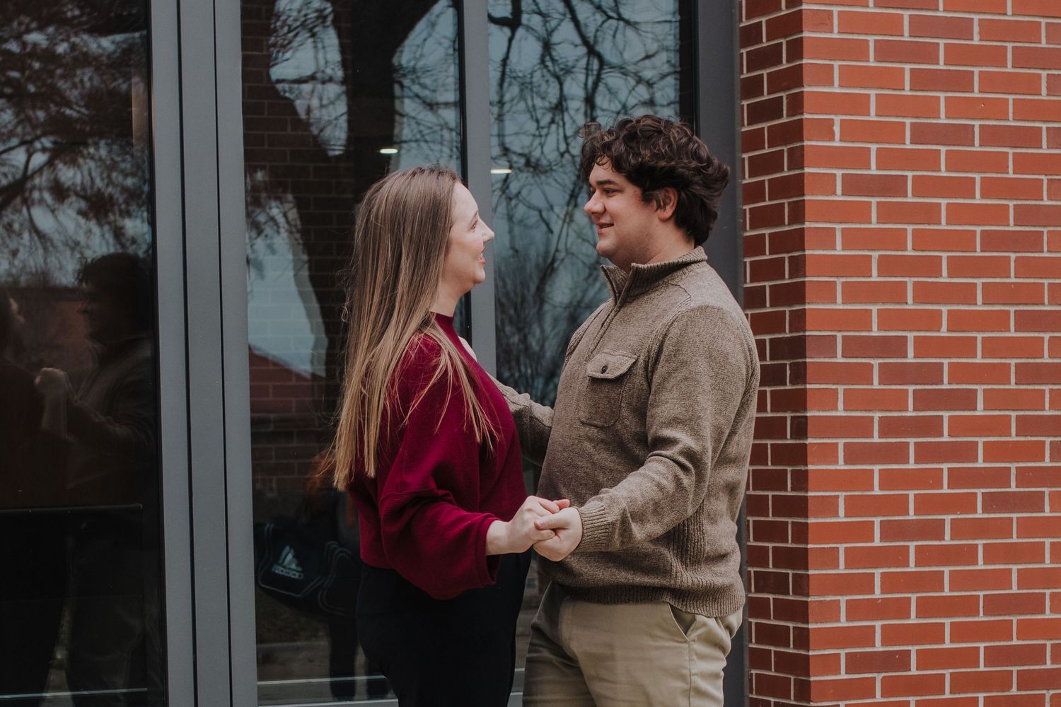 Young couple holding hands and smiling at each other outside a brick building.