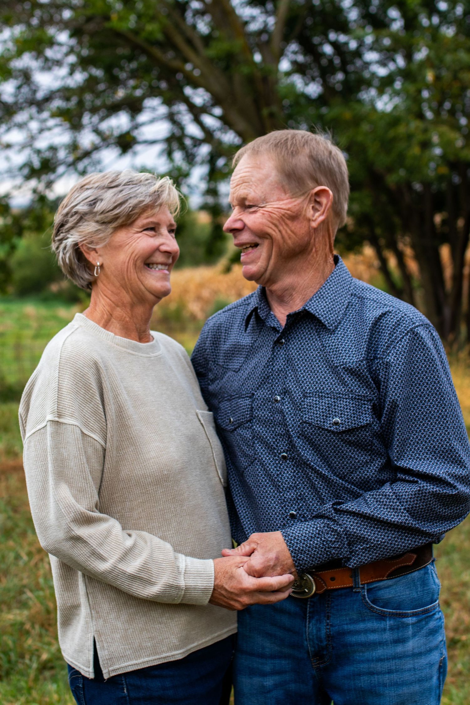 Smiling senior couple holding hands and laughing together outdoors in a lush green park setting.