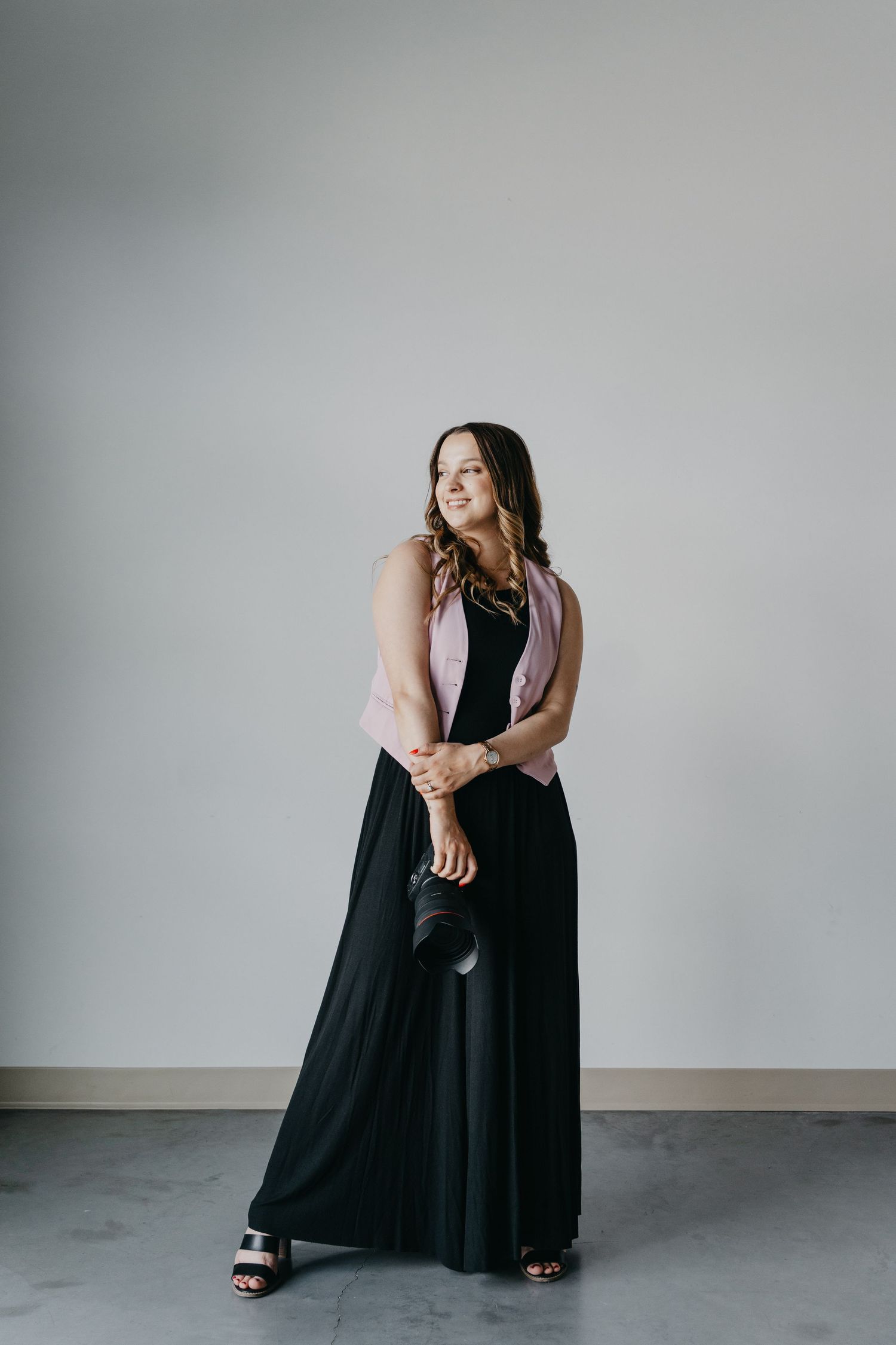 A person poses in a full-length black maxi dress with a pink cardigan against a minimalist gray backdrop.