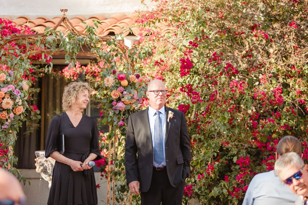 A garden wedding ceremony with bright red bougainvillea climbing the white stucco walls.