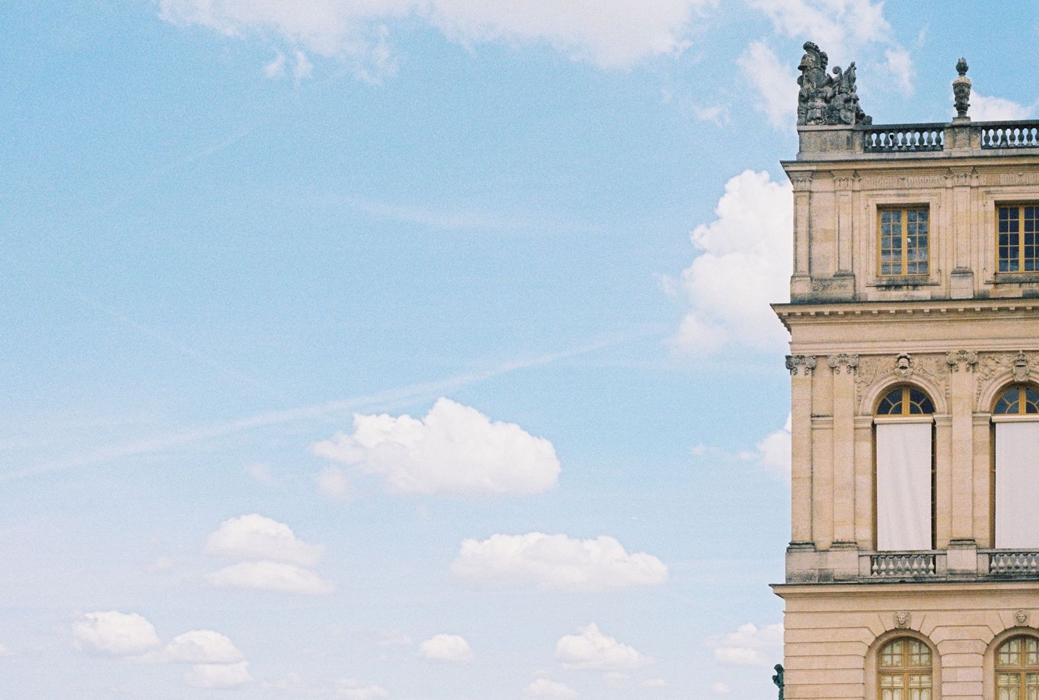 Ornate classical architecture detail of a grand palace against blue summer sky with white clouds.