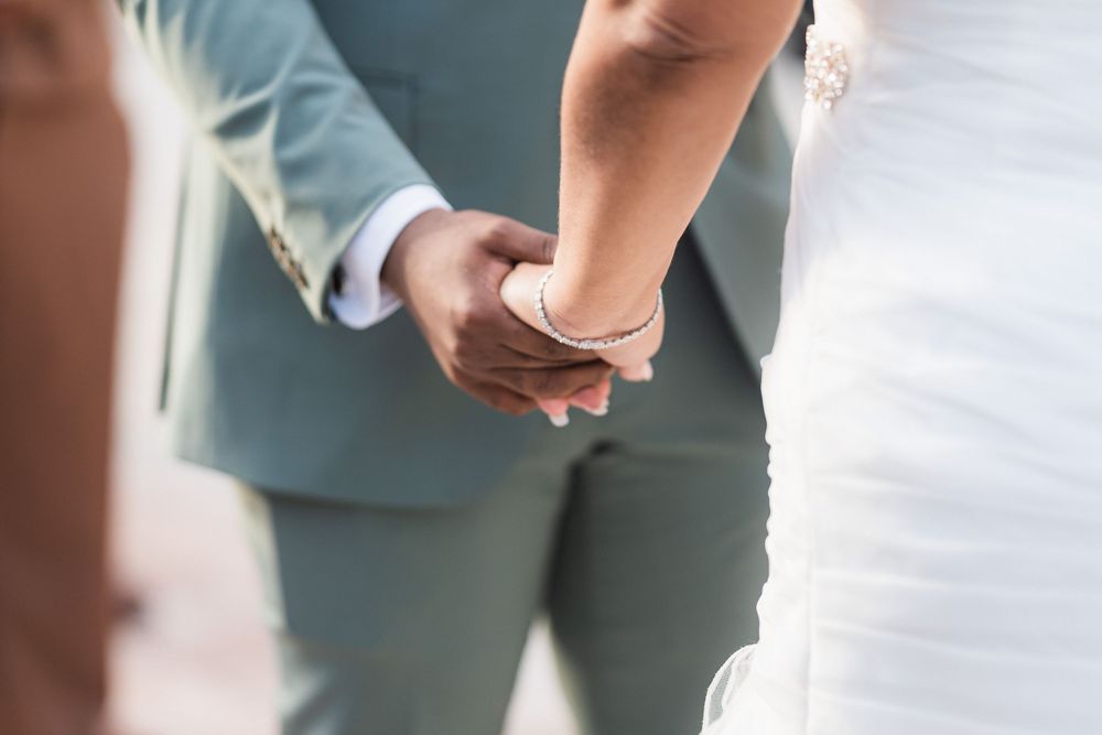 A close-up view of two people holding hands during a wedding ceremony, wearing formal attire.