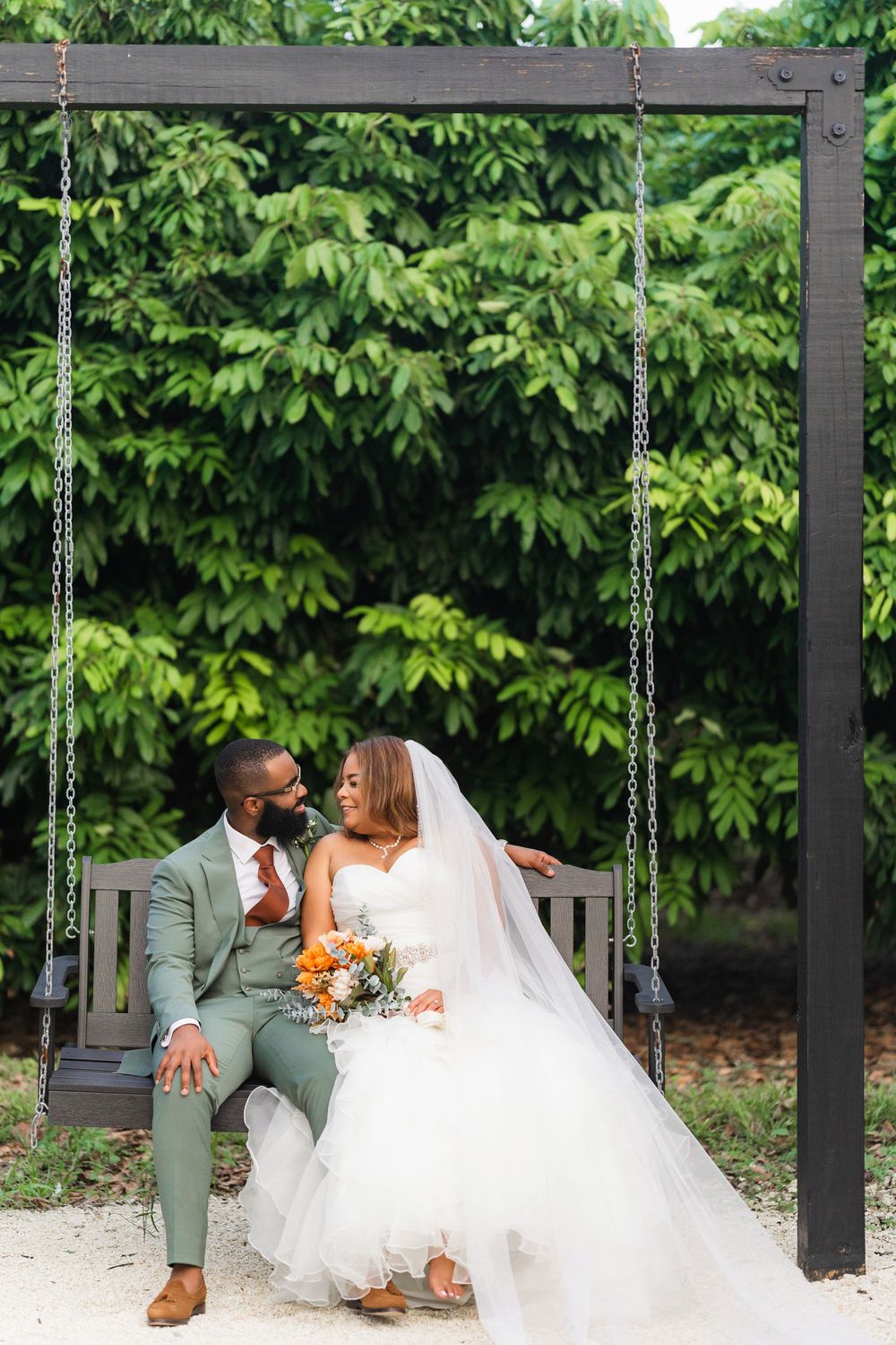 A couple shares an intimate moment on a wooden swing decorated with greenery and flowers.